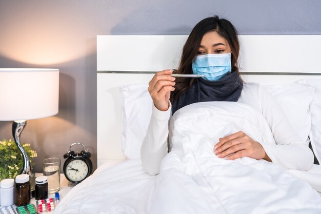 Sick woman in medical mask using thermometer to checking temperature, coronavirus pandemic concept.