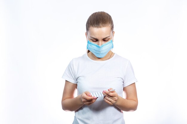 Sick woman in protective medical surgical mask with a thermometer and pills in her hand is treated for the virus. Self-isolation and medication