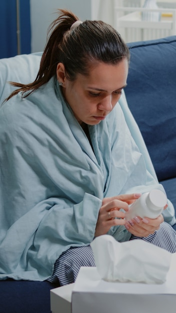 Sick woman reading label on bottle of pills and medicaments