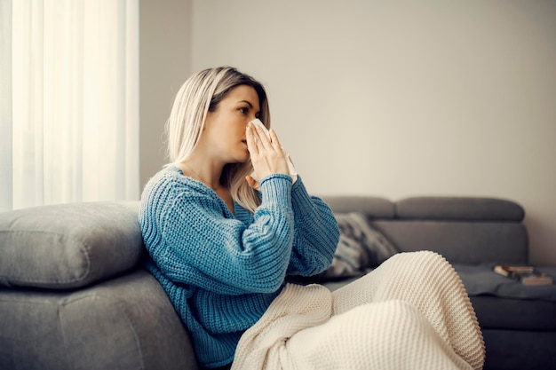 A sick woman sitting at home and blowing the nose