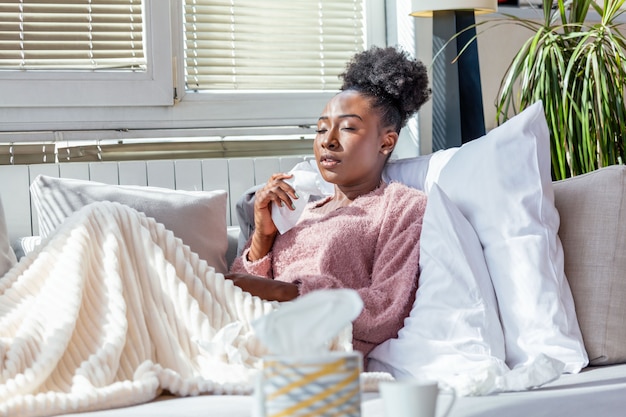 Sick woman on a sofa blowing her nose