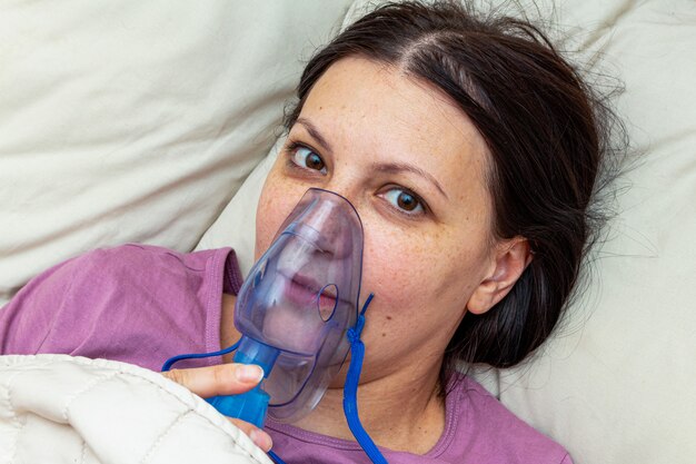 Photo sick woman suffers with viral flu in bed in a inhalation mask