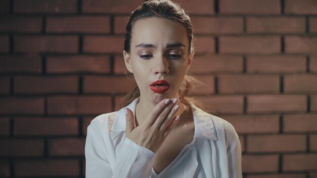 Sick woman touching sore throat and nose during a cold disease in brick studio