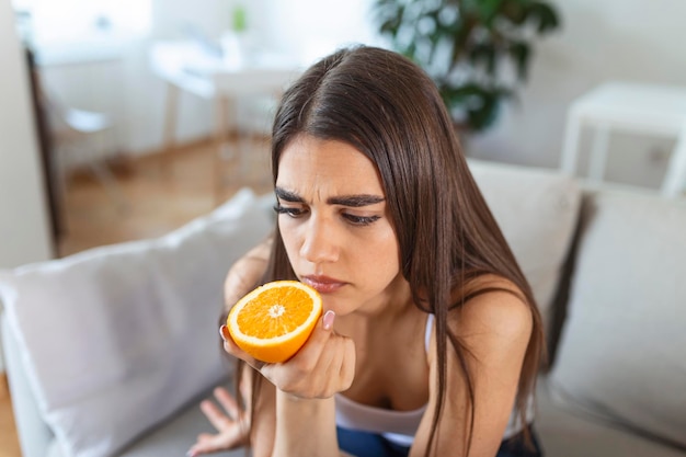 Photo sick woman trying to sense smell of half fresh orange has symptoms of covid19 corona virus infection loss of smell and taste one of the main signs of the disease