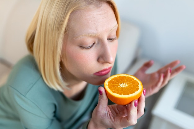 Sick woman trying to sense smell of half fresh orange has\
symptoms of covid19 corona virus infection loss of smell and taste\
one of the main signs of the disease