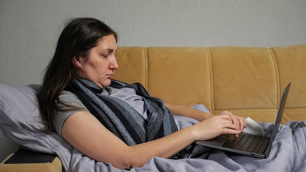 Sick woman with runny nose works distantly using laptop