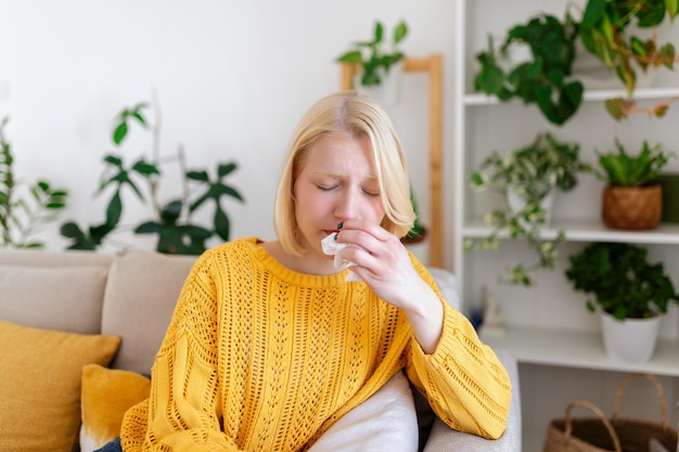 Sick womanfluwoman caught cold sneezing into tissue headache\
virus medicines young woman infected with covid 19 blowing her nose\
in handkerchief sick woman with a headache sitting on a sofa