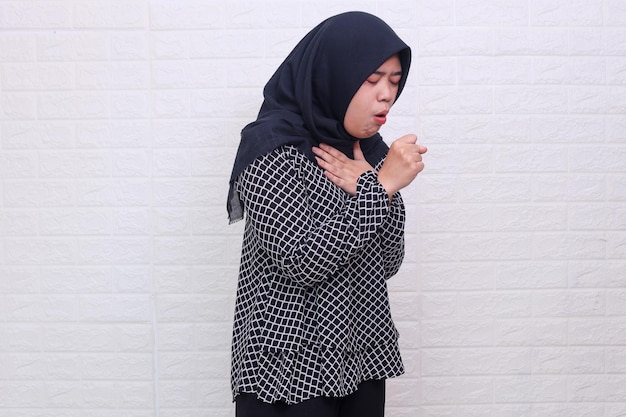 ヒジャブを着た病気の若いアジア系イスラム教徒の女性が体調不良を感じ、風邪や気管支炎の症状として咳をする