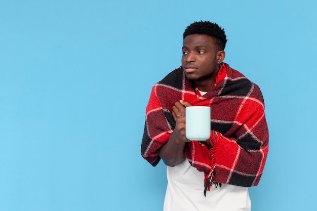 Photo sick young guy african american holding drink suffers from fever and is covered with warm plaid