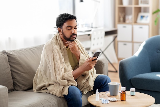 sick young man in blanket with smartphone at home