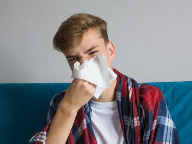 Sick young man blowing his nose in tissue paper