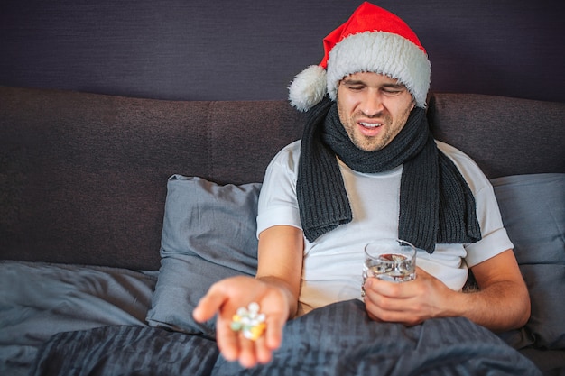 Sick young man in Christmas red hat sits on the bed