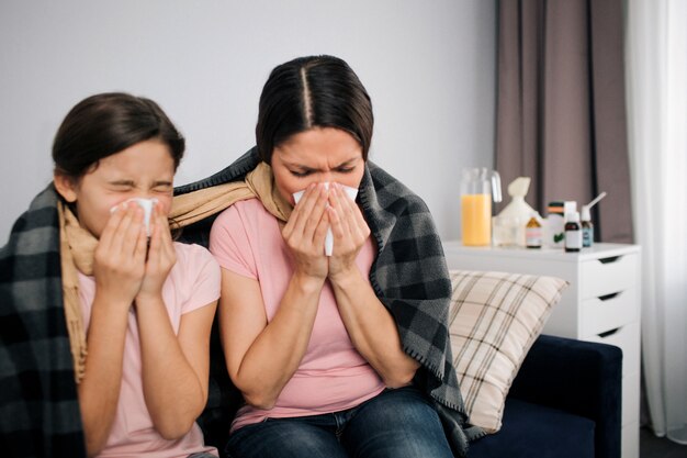 Sick young woman and girl sit together on couch