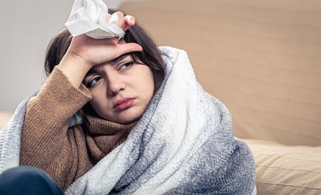 A sick young woman is sitting at home wrapped in a blanket