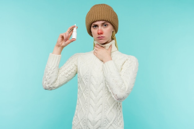 Sick young woman in scarf and hat use nasal spray