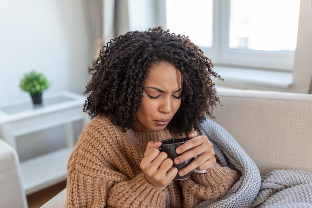 Sick young woman sitting at home in bed with hot cup of tea and\
handkerchief seasonal colds cough runny nose viral infections home\
treatment