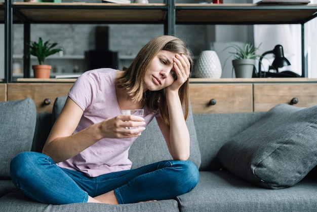 写真 水のガラスでソファーに座って病気の若い女性