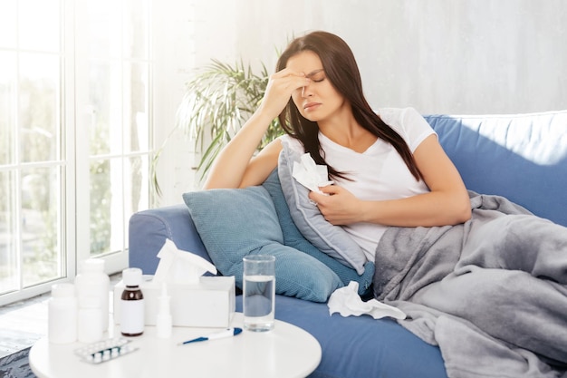 Sick young woman touching her face and holding a napkin while lying with closed eyes