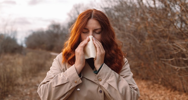 Sick young woman with handkerchief runny nose cold infection at city autumn park healthcare cold all...