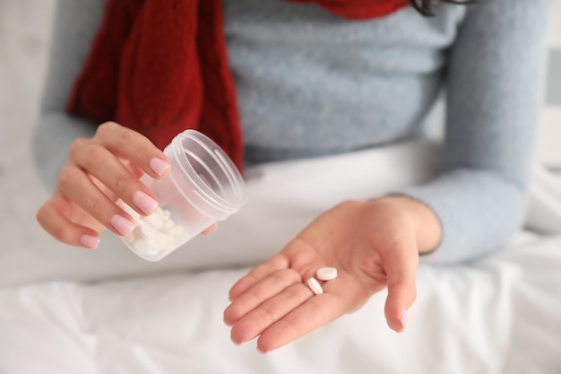 Sick young woman with pills at home, closeup