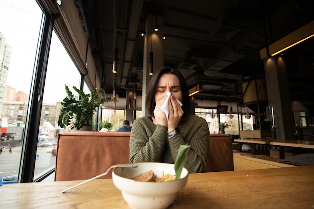 Sick young woman with runny nose came to a cafe.