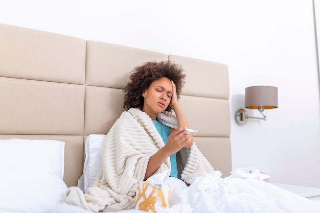 Concetto di problema di virus stagionale di malattia donna malata con influenza sdraiata sul letto guardando la temperatura sul termometro donna malata sdraiata a letto con febbre alta influenza fredda coronavirus covid19