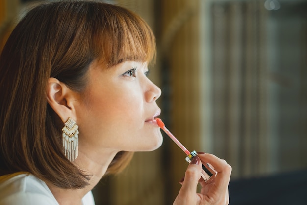 Side of beautiful young woman putting on red lipstick gloss.