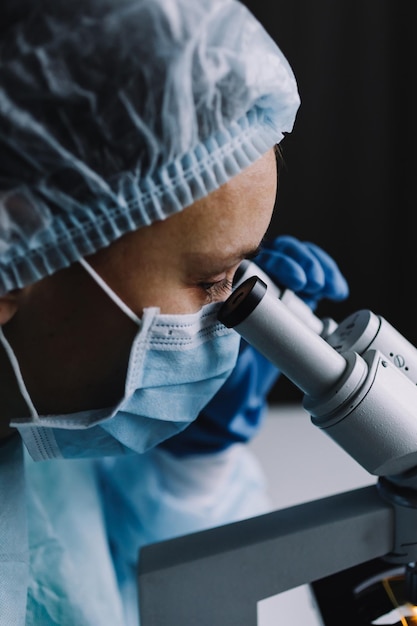 Side close up view of scientist in uniform looking at microscope in lab