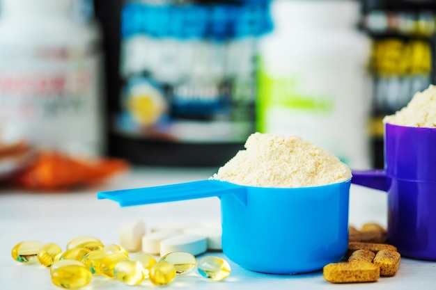 Side closeup view of blue and purple measure dishes with protein powder and sport pills around on the white table