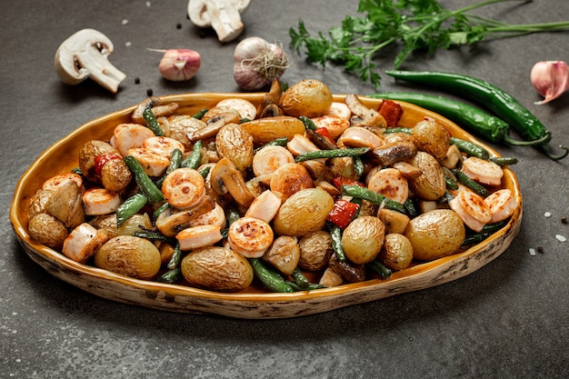 Side dish of baked vegetables asparagus bean, pepper, mushrooms and sausage, vertical orientation. Gray stone background. Top view