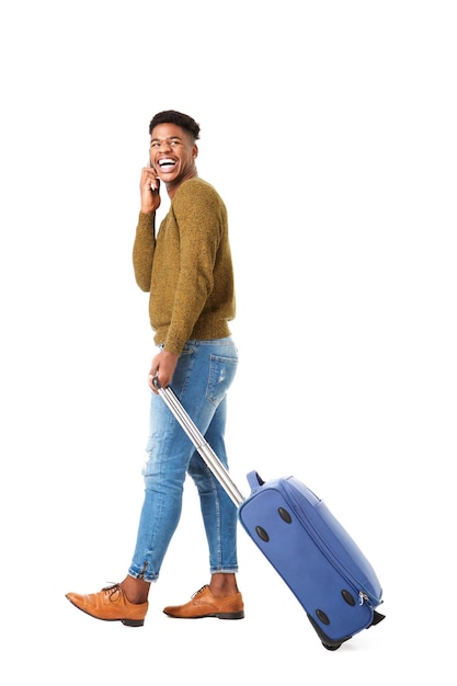 Side of happy young african american travel man walking with mobile phone and suitcase against isolated white background