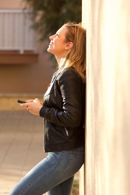 Side of happy young woman holding mobile phone