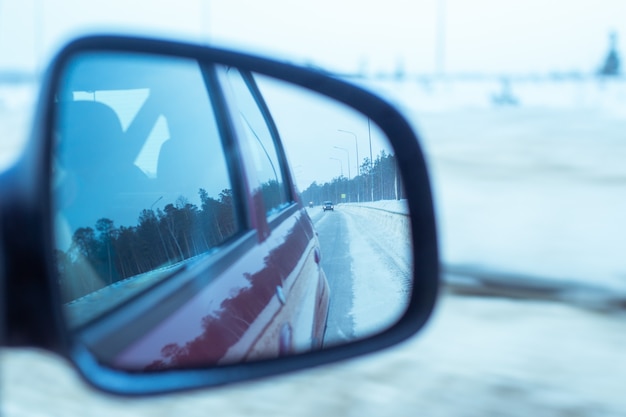 In the side mirror of the car the road and transport are visible in winter