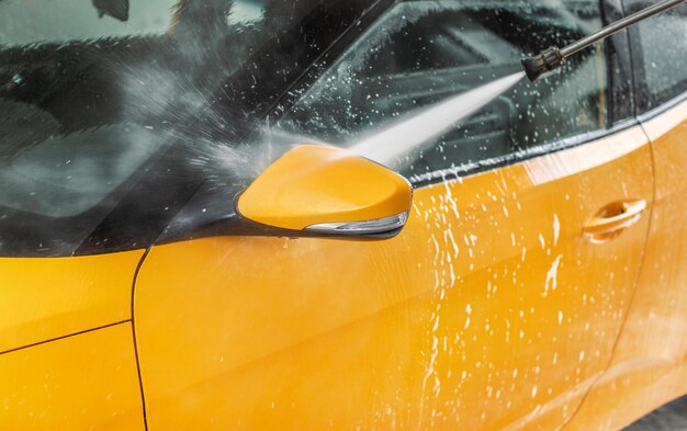 Side mirror of car washed in self serve carwash, jet water spraying from high pressure hose nozzle.