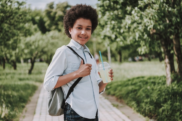 Foto laterale del succo sorridente della tenuta del ragazzo in parco.