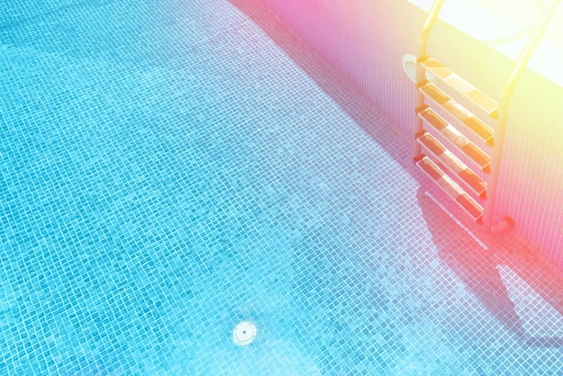 Side of the pool with stairs and tiles with empty copy space and sun glare