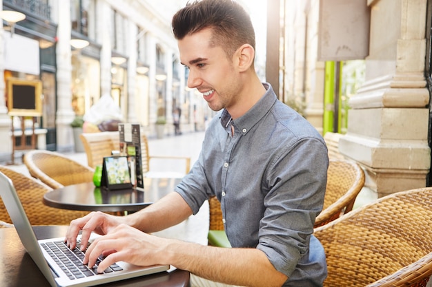 Side portrait of handsome happy man working at cafe typing on laptop