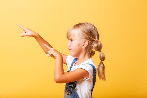 Ritratto laterale di una bambina. lei è carina carina attraente ragazza bionda allegra che indica