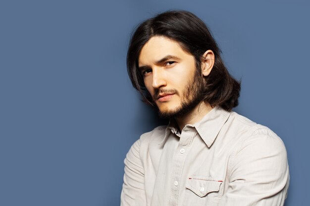 Side portrait of young serious man with long hair looking away. Background of blue color with copy space.