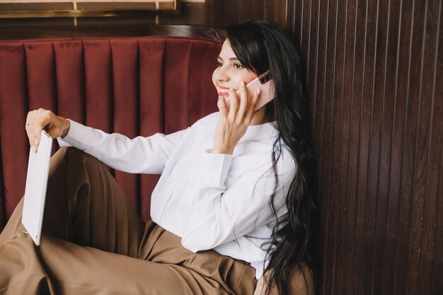 Side profile photo of a business woman talking on the phone businesswoman sitting on a sofa in a cozy cafe