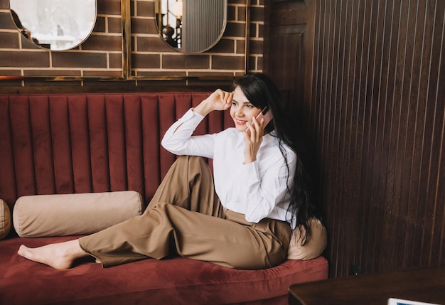 Боковое фото бизнес-леди, разговаривающей по телефону, деловой женщины, сидящей на диване в уютном кафе