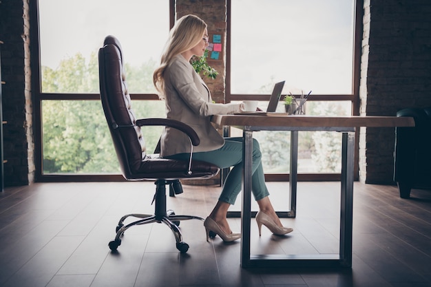 Side profile of pondering pensive business lady in heeled shoes staring into screen of laptop