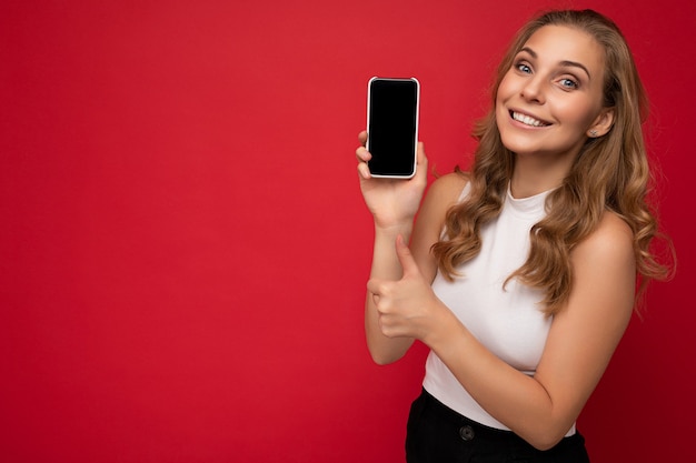 Profilo laterale di sorridente divertente bella giovane donna bionda che indossa la maglietta bianca isolata sul rosso