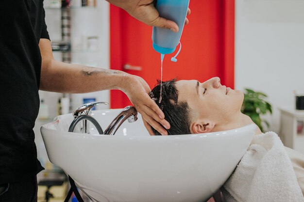 Foto tiro laterale delle mani del barbiere che fanno cadere lo shampoo nei capelli del suo cliente