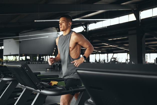 side shot of athletic man running on treadmill preforming warmingup run routine exercise in gym