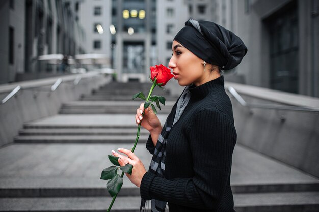 Side shot of young arabian woman stand on steps and hold red rose in hands.