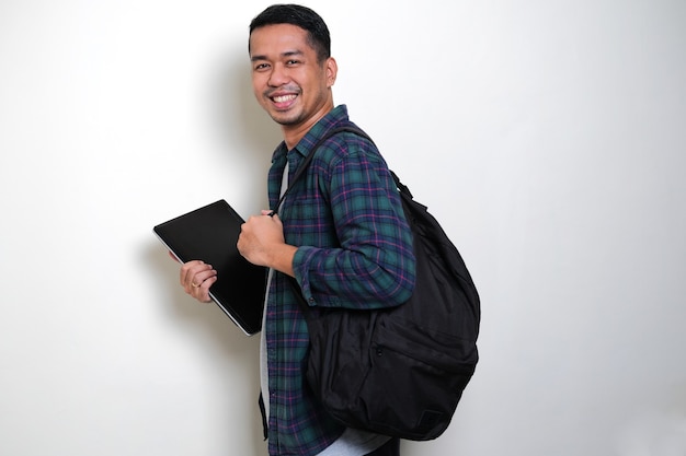 Side view of Adult Asian man bring backpack and laptop showing happy face expression