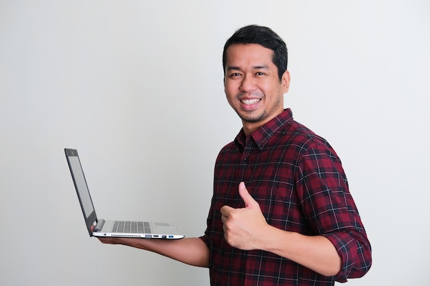 Side view of Adult Asian man smiling confident and give thumb up while holding a laptop computer