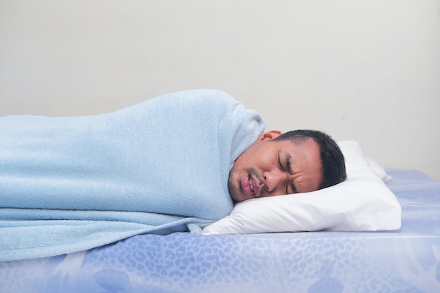 Side view of adult Asian man use blanket when sleeping with sick expression