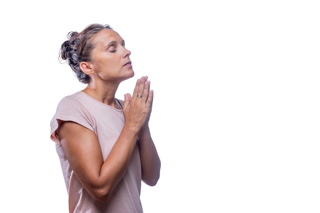 Side view of an adult woman with her eyes closed praying with hands clasped on a white background with copy space.